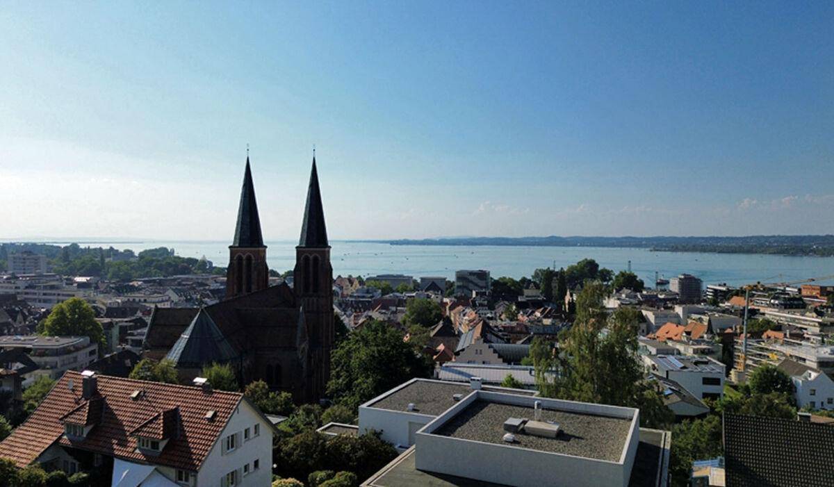 Weitläufige Luftaufnahme einer Stadt mit einer markanten Kirche und einem großen See am Horizont.