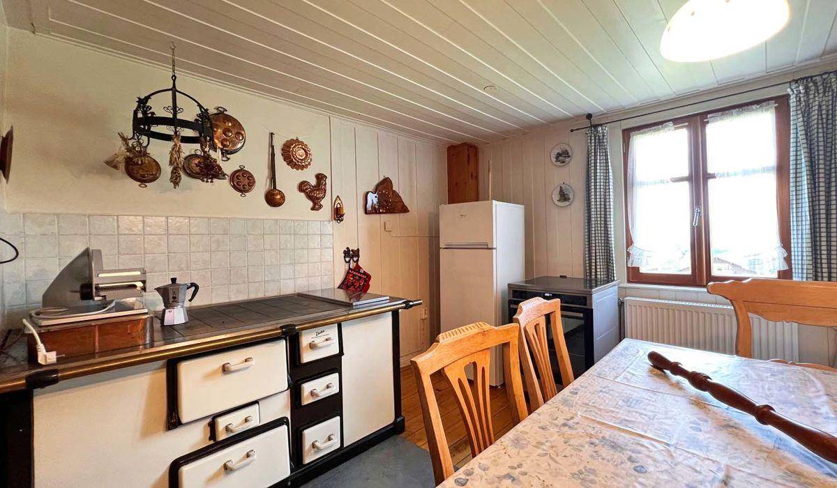 Traditionelle Küche mit Holzvertäfelung, altem Herd und einem Esstisch am Fenster.
