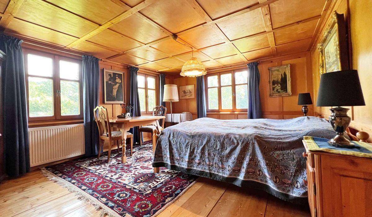 Gemütliches Schlafzimmer im Alpenstil mit Holztäfelung, Doppelbett und mehreren Fenstern.