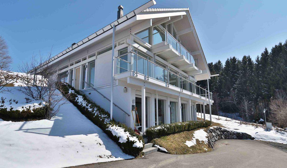 Modernes Wohnhaus mit großen Fensterfronten und Terrassen, eingebettet in eine schneebedeckte Hanglage.