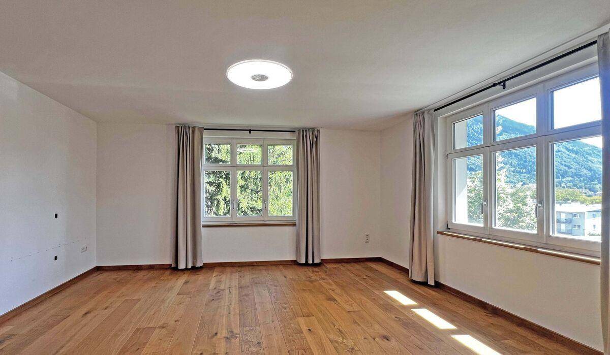 Renoviertes Zimmer mit neuem Holzboden und großen Fenstern, die viel Licht hereinlassen.