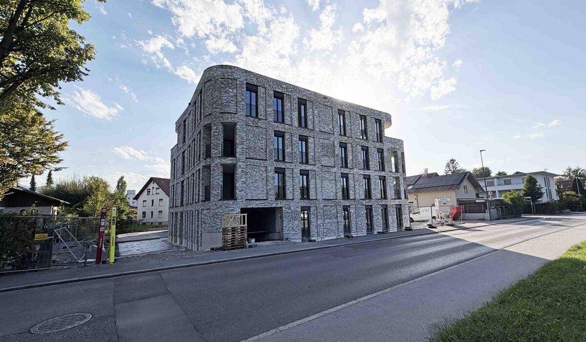 Neubau mit markanter grauer Ziegelfassade und abgerundeter Ecke an einer Straße.