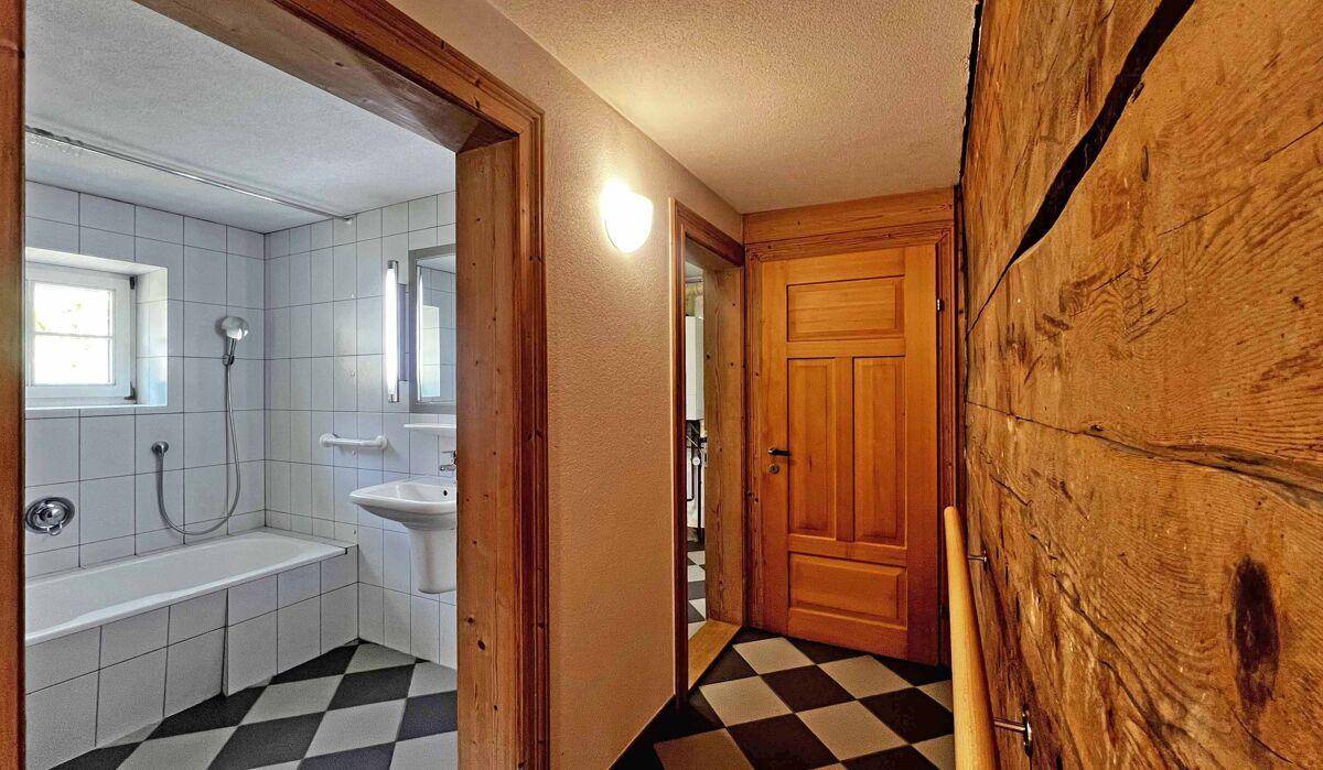 Flur mit Holzwänden und schwarz-weißem Fliesenboden, angrenzend an ein Badezimmer.