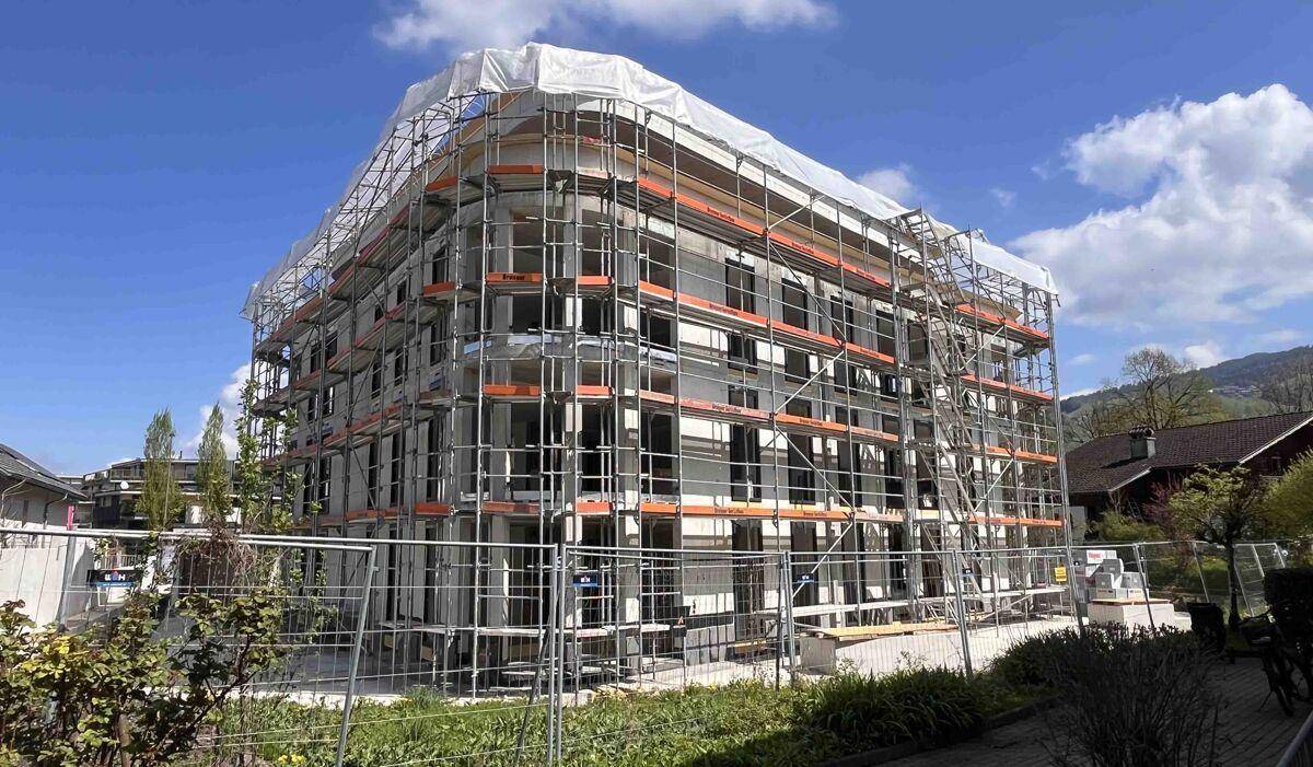Neubau in Bauphase mit Gerüst und Schutzplane unter blauem Himmel.