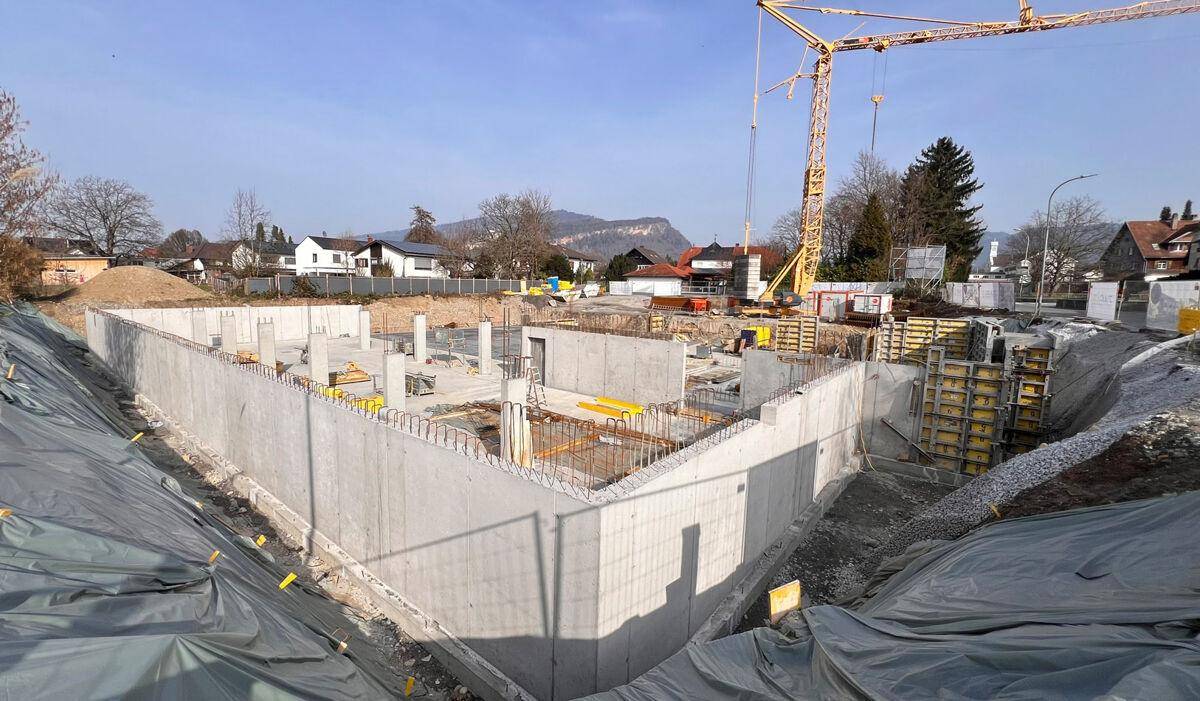 Baustelle mit Betonfundamenten und einem Baukran unter klarem Himmel.