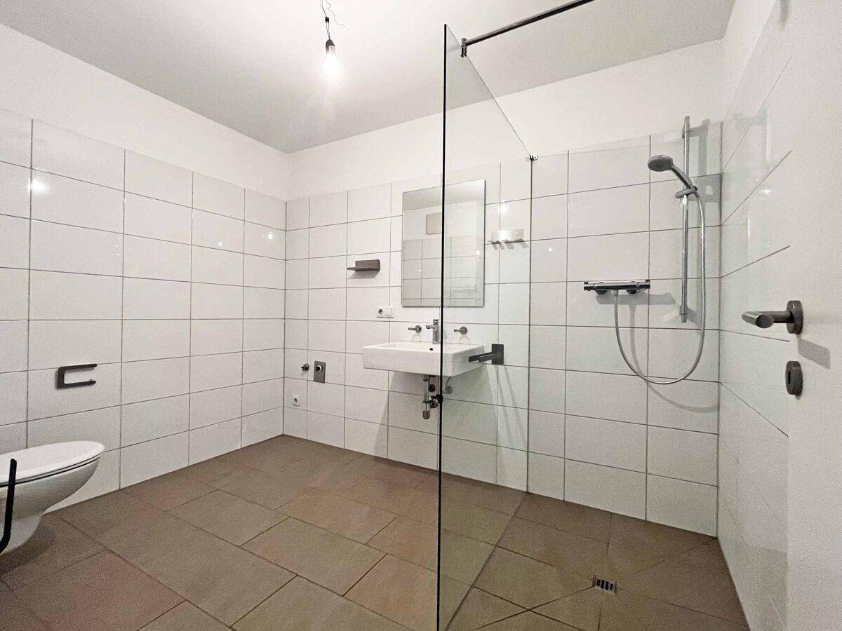 Modernes Badezimmer mit begehbarer Dusche, Wand-WC und hellen Fliesen.