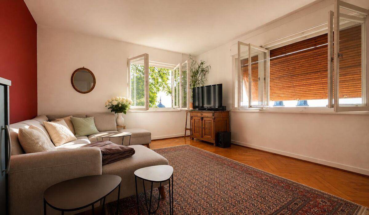 Geräumiges Wohnzimmer mit bequemer Couch, Fernseher und Fenstern mit Holzjalousien für Privatsphäre.