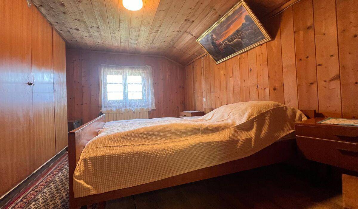 Gemütliches Schlafzimmer mit Holzwänden, Holzboden und einem Fenster mit Blick ins Grüne.