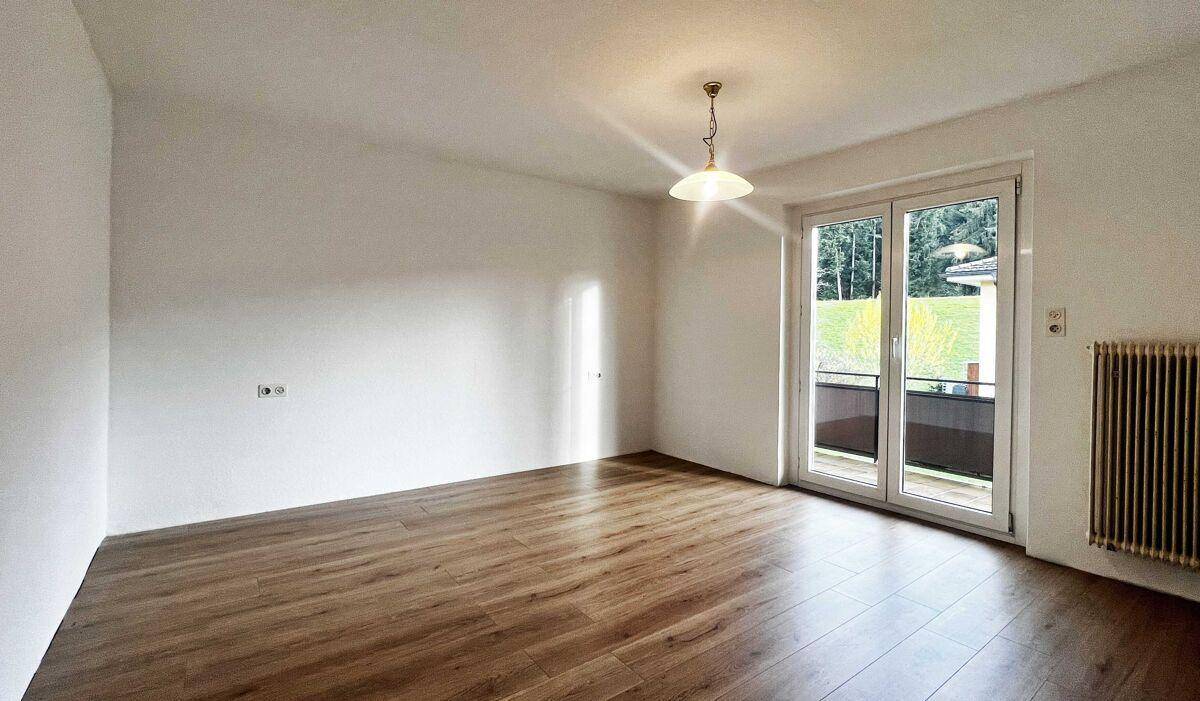 Geräumiger, heller Raum mit Holzfußboden und Zugang zu einem Balkon.
