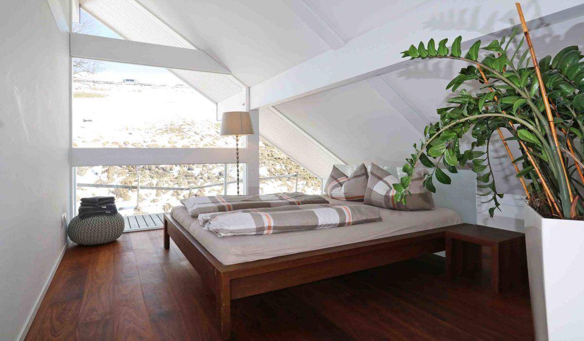 Schlafzimmer im Dachgeschoss mit Holzboden, großen Fenstern und schräger Decke.