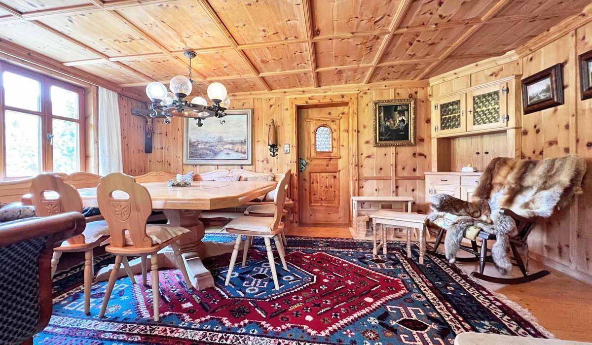 Rustikaler Essbereich mit Holztisch, Stühlen und einem traditionellen Teppich in einem holzgetäfelten Raum.