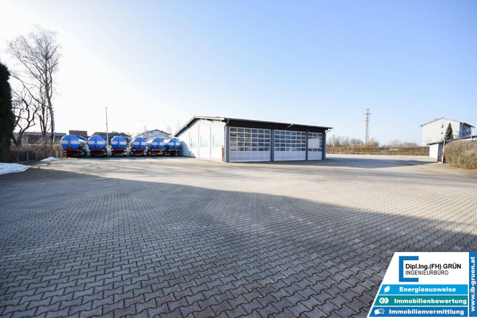 Weitläufiger gepflasterter Vorplatz vor der Halle mit abgestellten Tankwagen unter blauem Himmel.