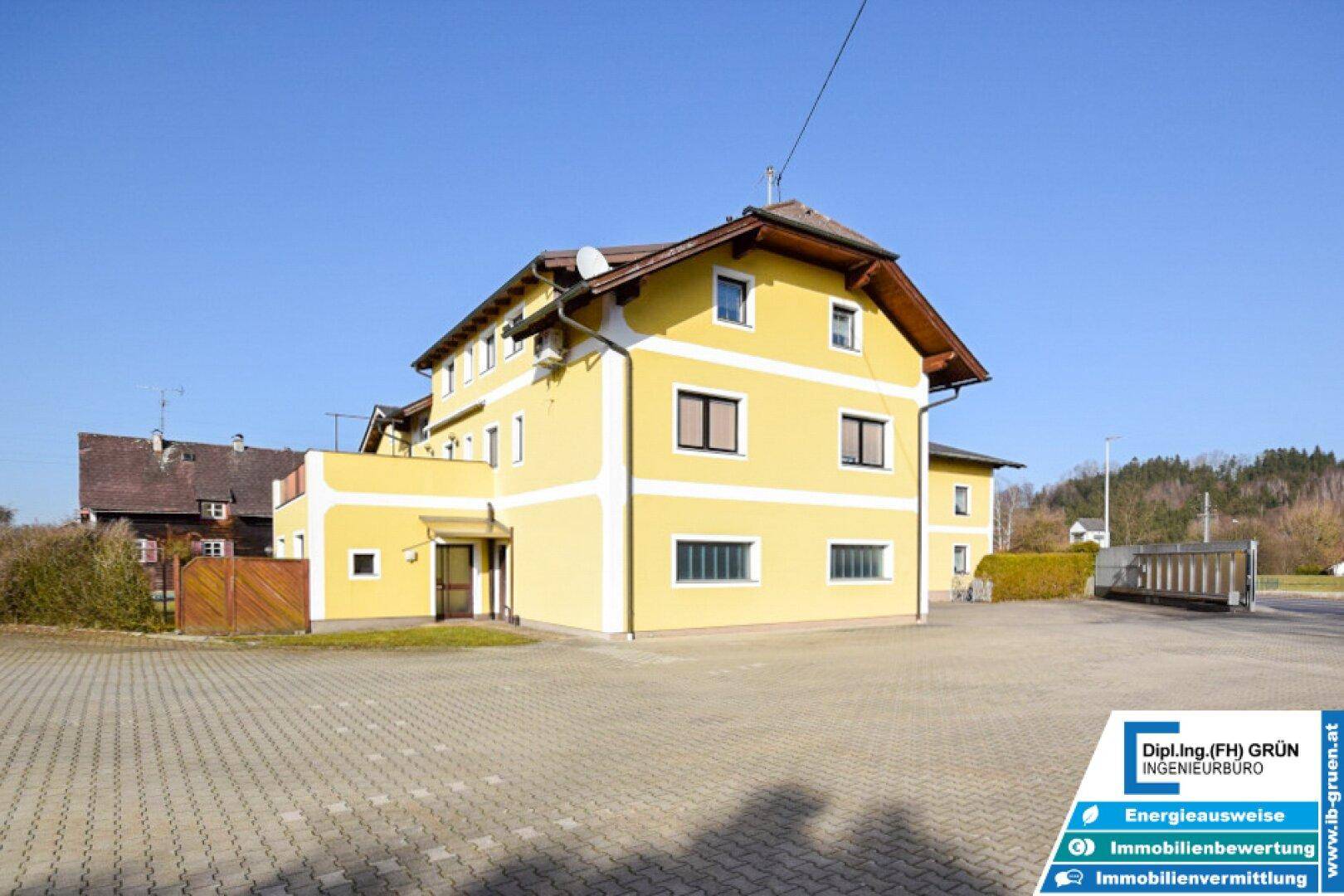 Seitenansicht des gelben Gebäudes mit Holzzaun und gepflastertem Bereich unter blauem Himmel.