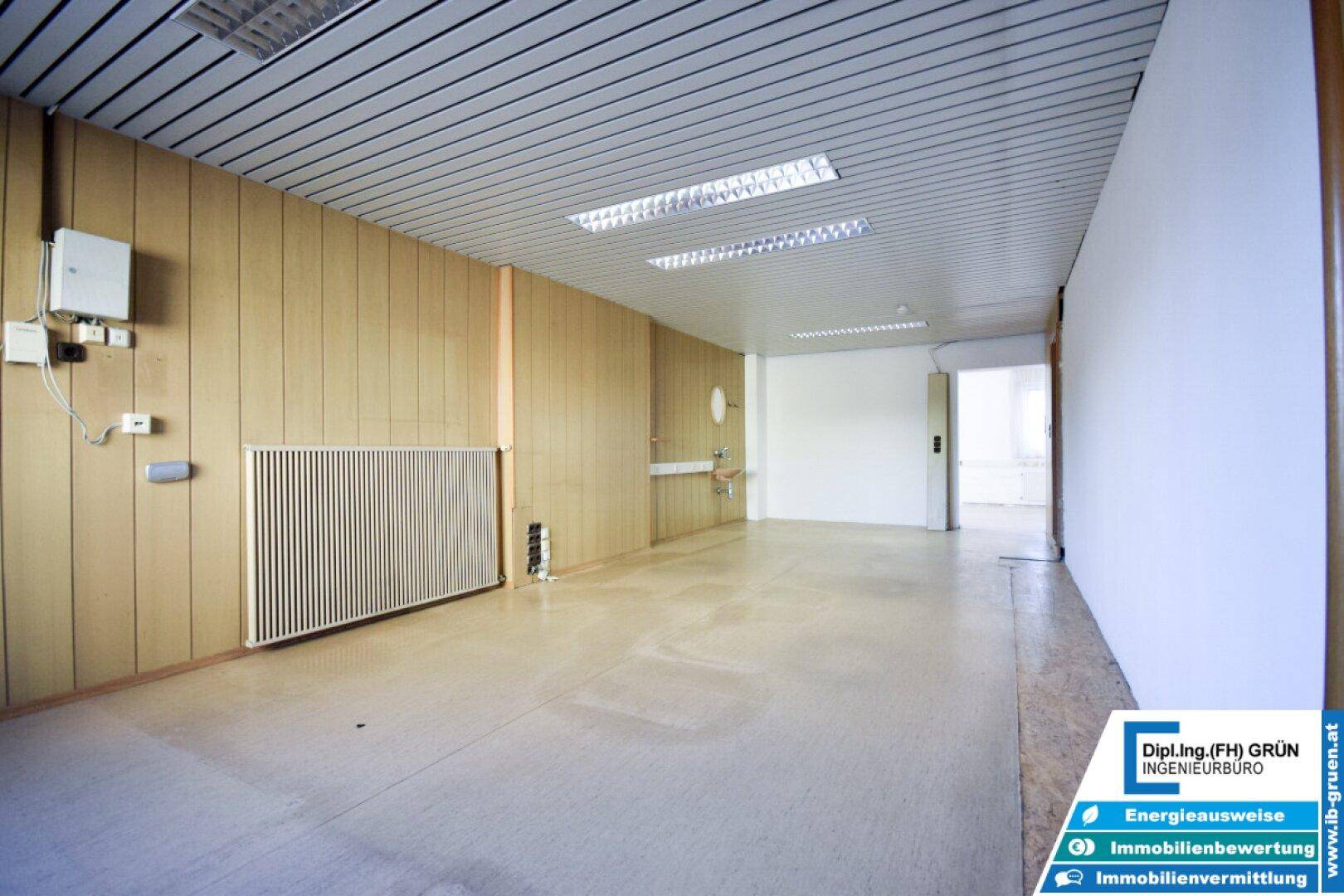 Geräumiger, leerer Raum mit Holzpaneelen an der Wand und Deckenbeleuchtung, ideal als Büro.