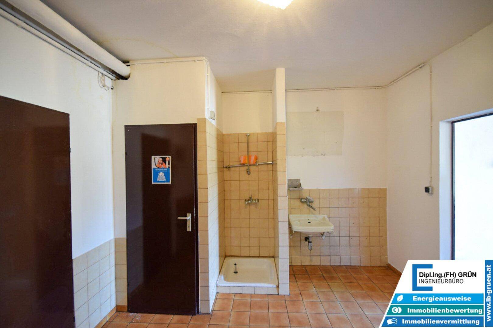 Einfacher Duschraum mit Terrakottafliesen, Duschbereich und kleinem Waschbecken.