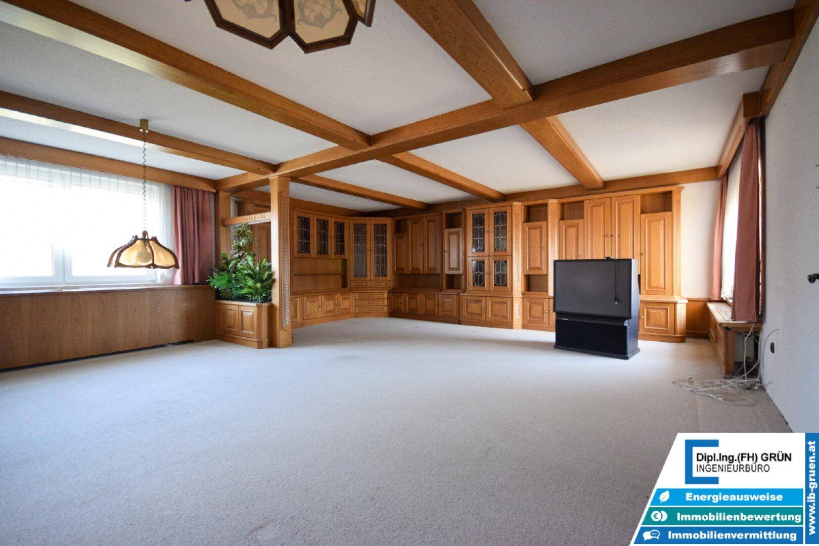 Geräumiges Wohnzimmer mit Teppichboden, Holzbalkendecke und eingebauten Holzschränken.
