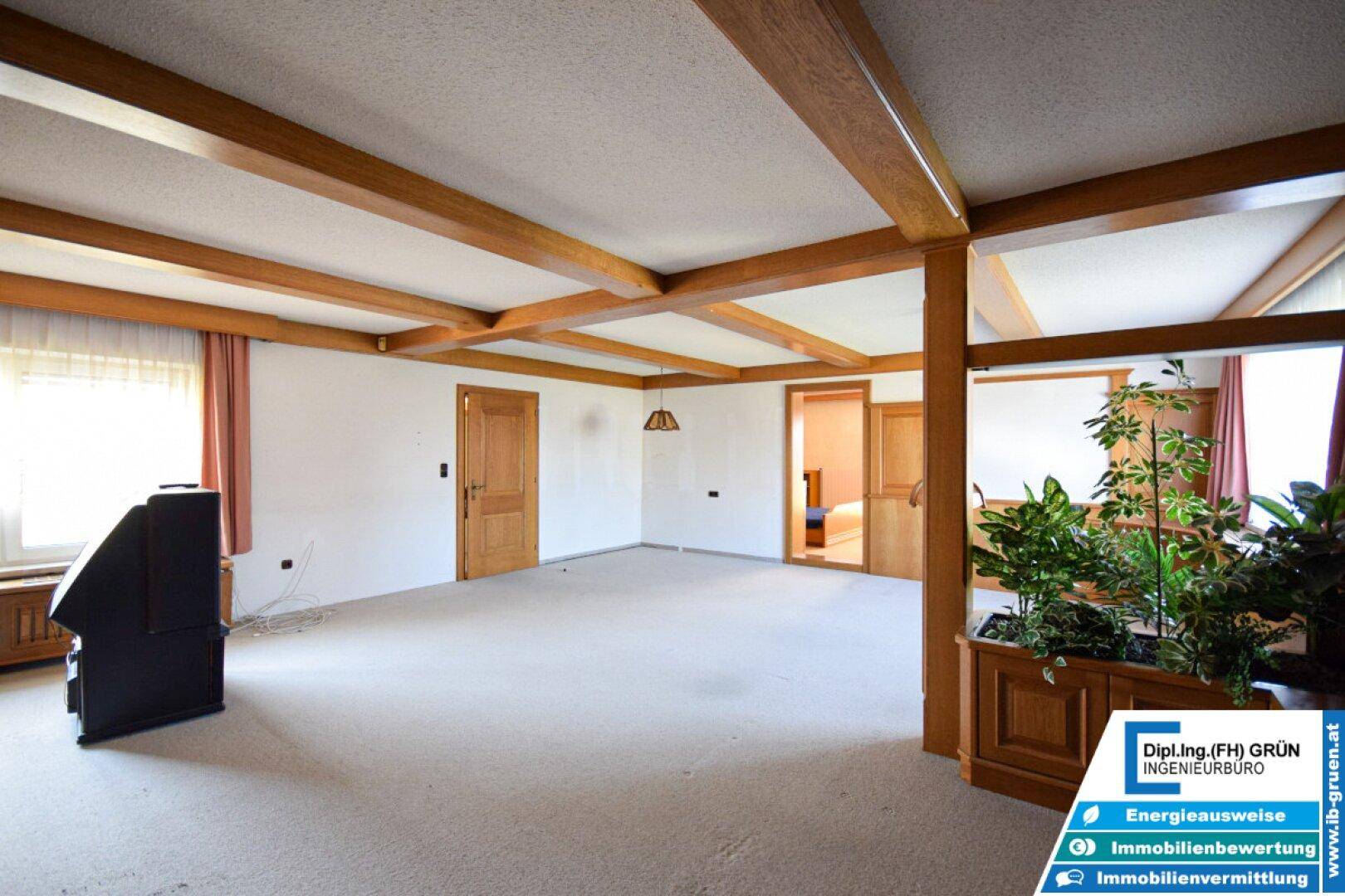 Helles Wohnzimmer mit Teppichboden, Holzbalkendecke und traditioneller Einrichtung.