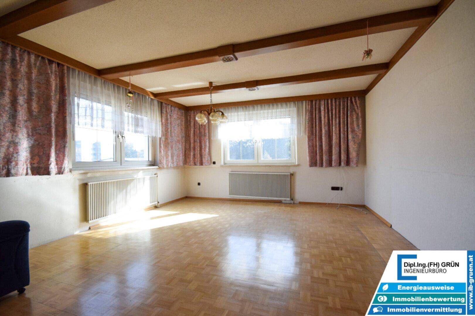 Helles Wohnzimmer mit Parkettboden, Holzbalkendecke und großen Fenstern.