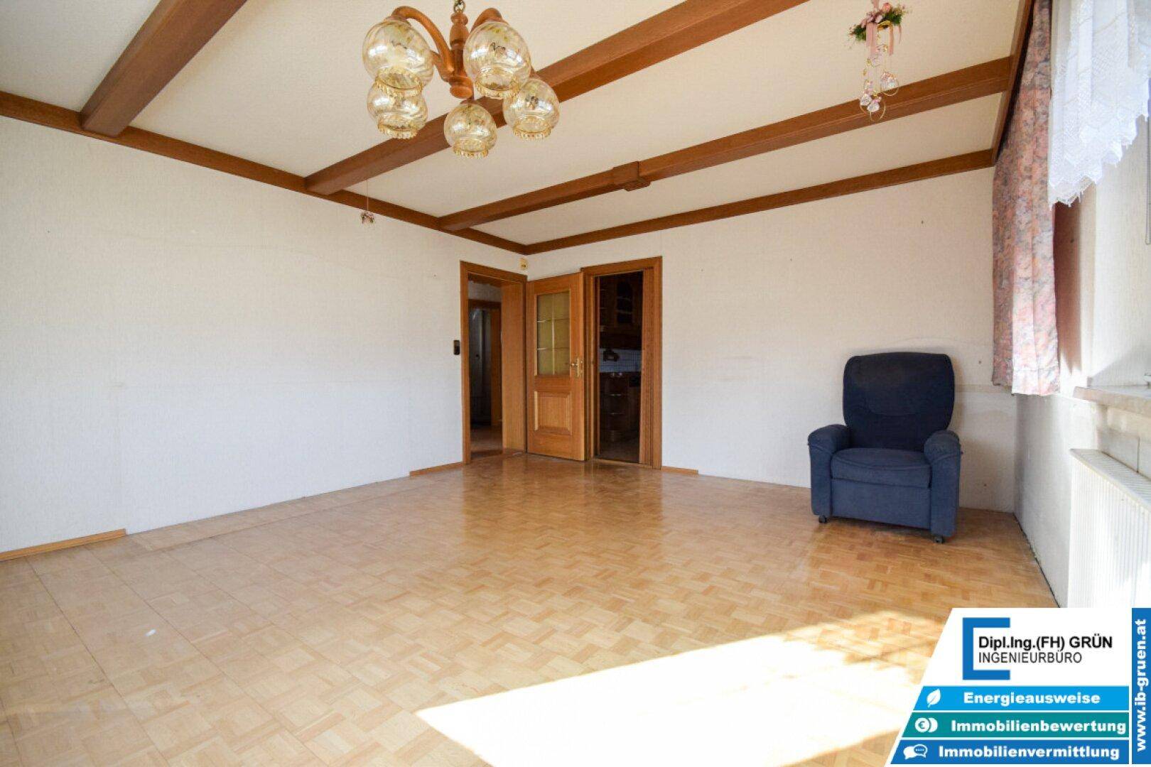Geräumiges Wohnzimmer mit Parkettboden, Holzbalkendecke und gemütlichem Sessel.