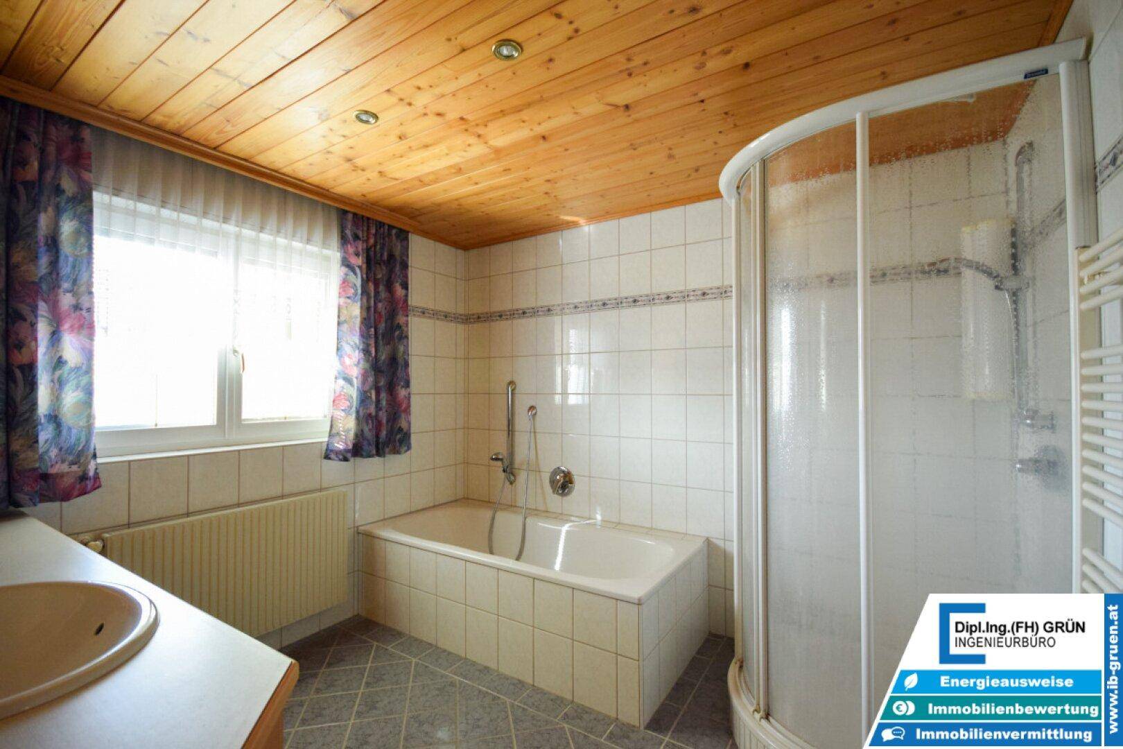 Badezimmer mit Badewanne, Eckdusche, Waschtisch und Holzdecke, hell gefliest.