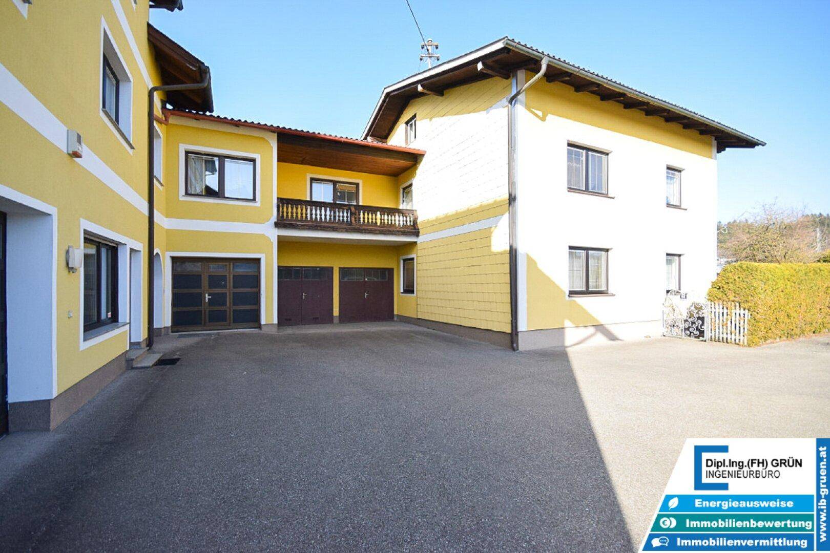 Gesamtansicht des gelben Hauses mit Garagen und Balkon an einem sonnigen Tag.