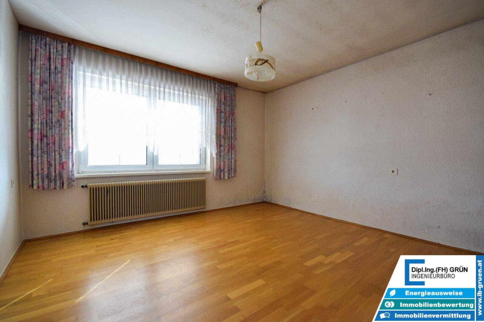 Heller, leerer Raum mit Laminatboden und großem Fenster.
