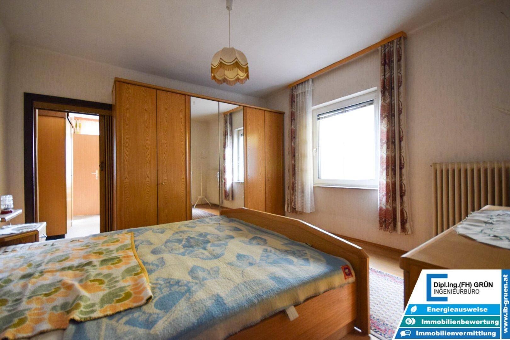 Schlafzimmer mit Bett, Kleiderschrank und Fenster.
