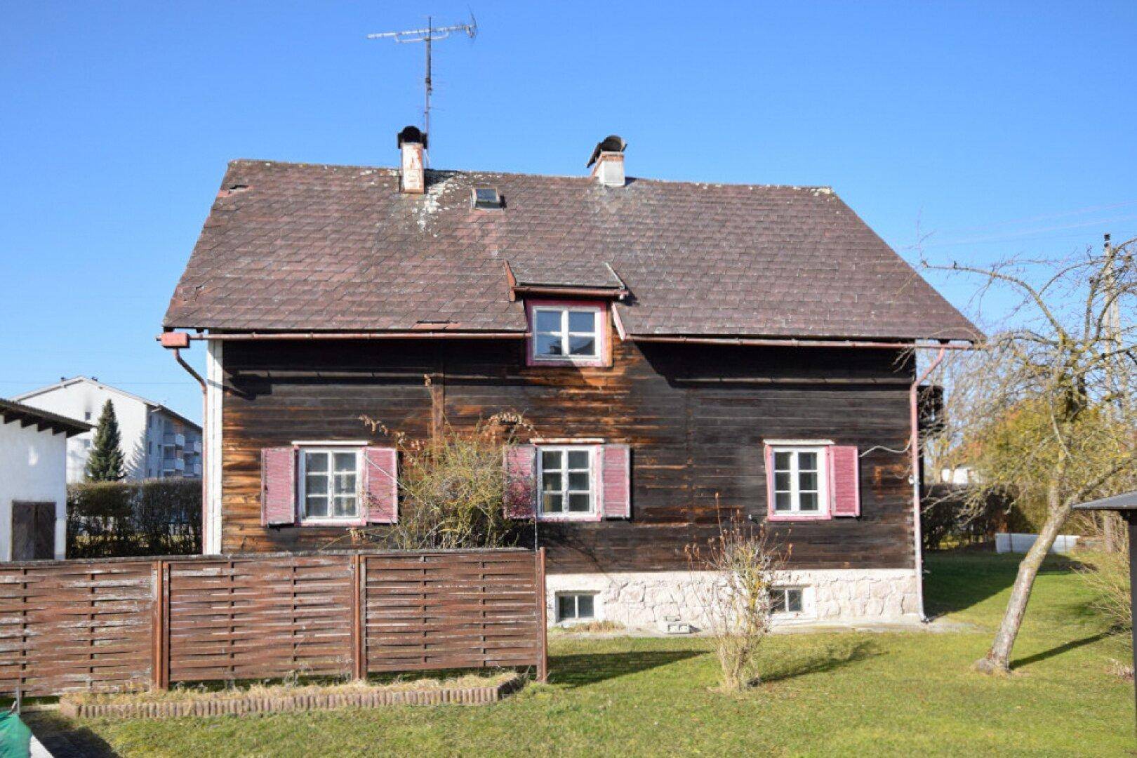 Vorderansicht eines traditionellen Holzhauses mit Satteldach und roten Fensterläden.