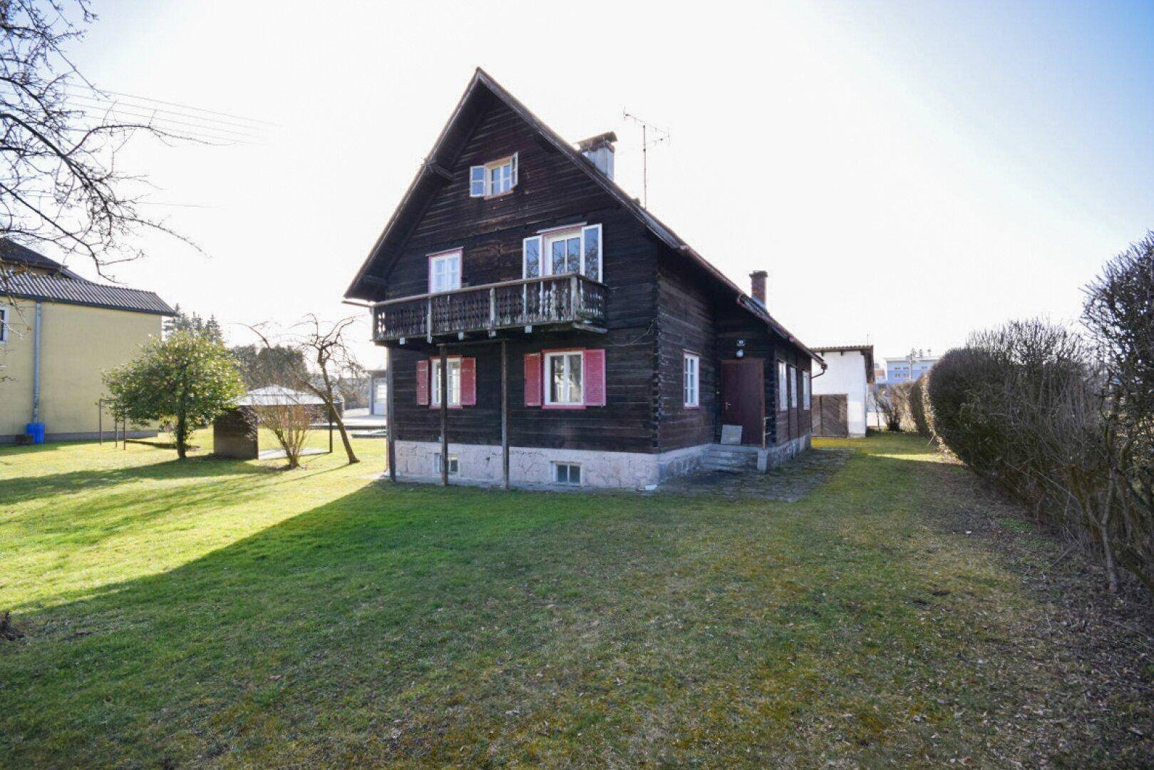 Traditionelles Holzhaus mit Balkon und weitläufigem Gartenbereich an einem sonnigen Tag.