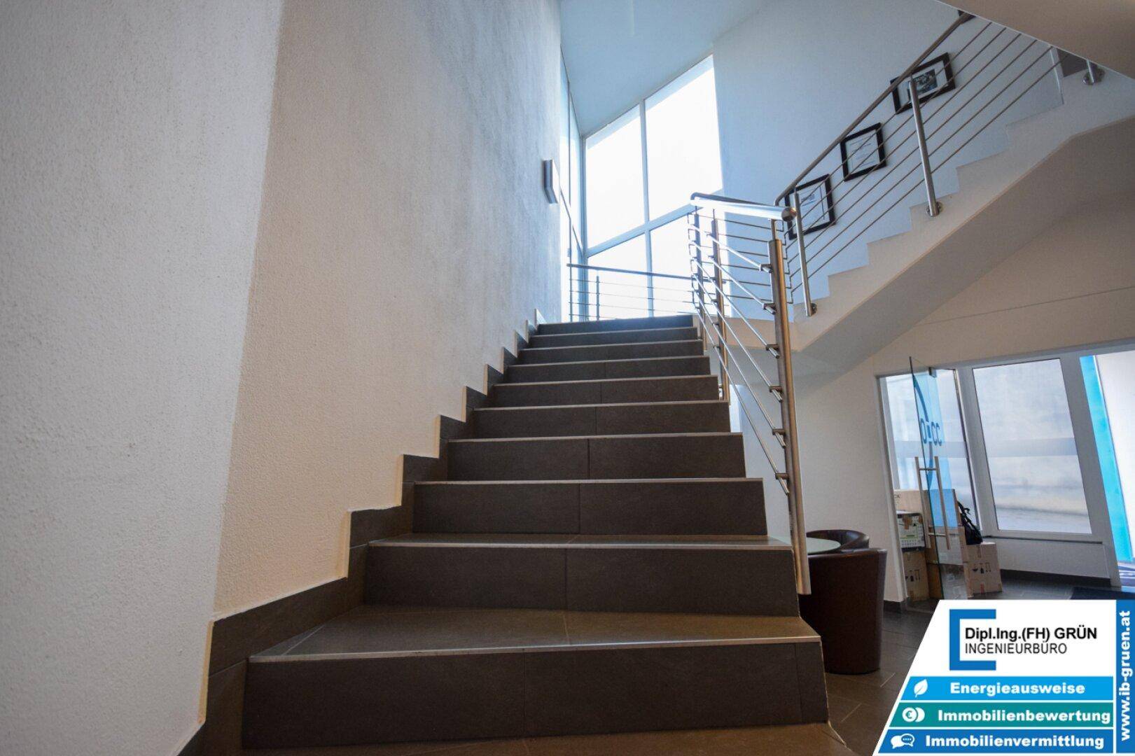 Moderne Treppe mit Fliesenstufen und Edelstahlgeländer, die zu den oberen Etagen führt.