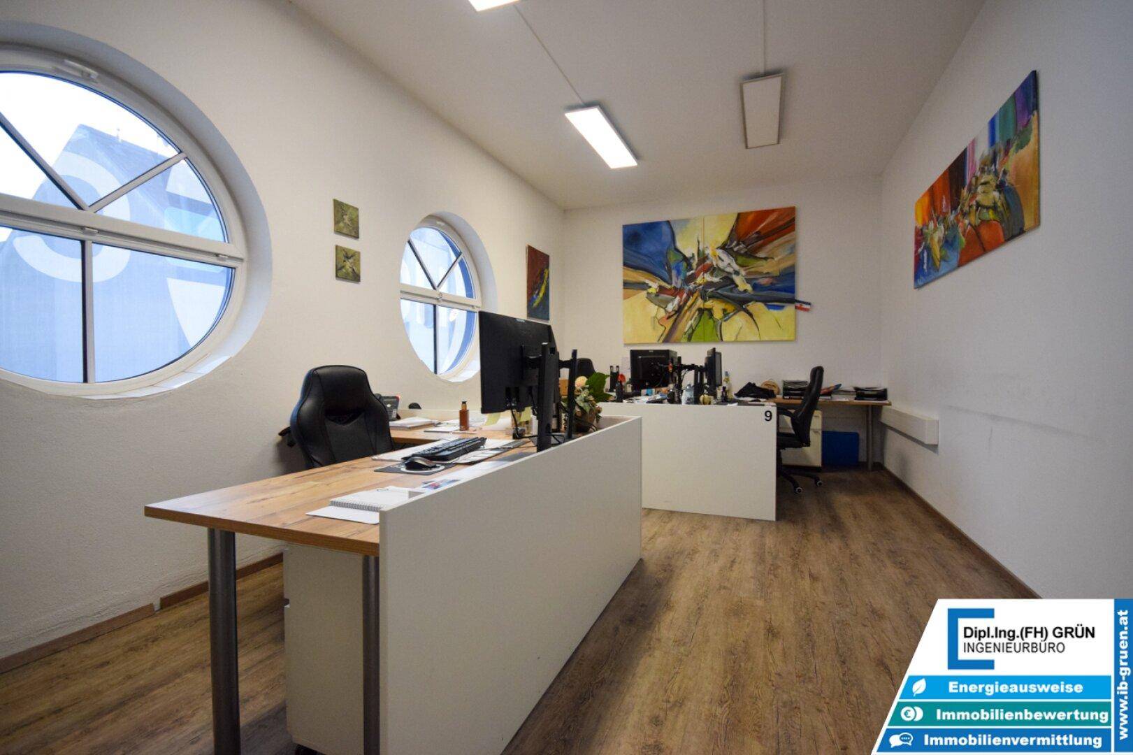 Büro mit runden Fenstern, Holzboden und mehreren Arbeitsplätzen in heller Atmosphäre.