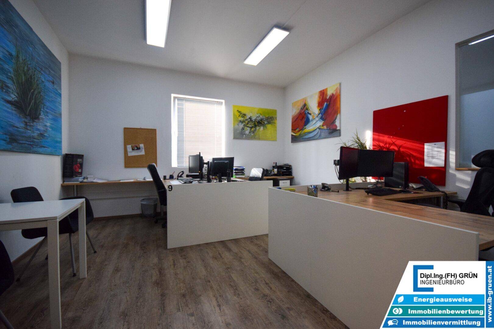 Helles Büro mit Holzboden, modernen Schreibtischen und farbigen Akzenten an den Wänden.