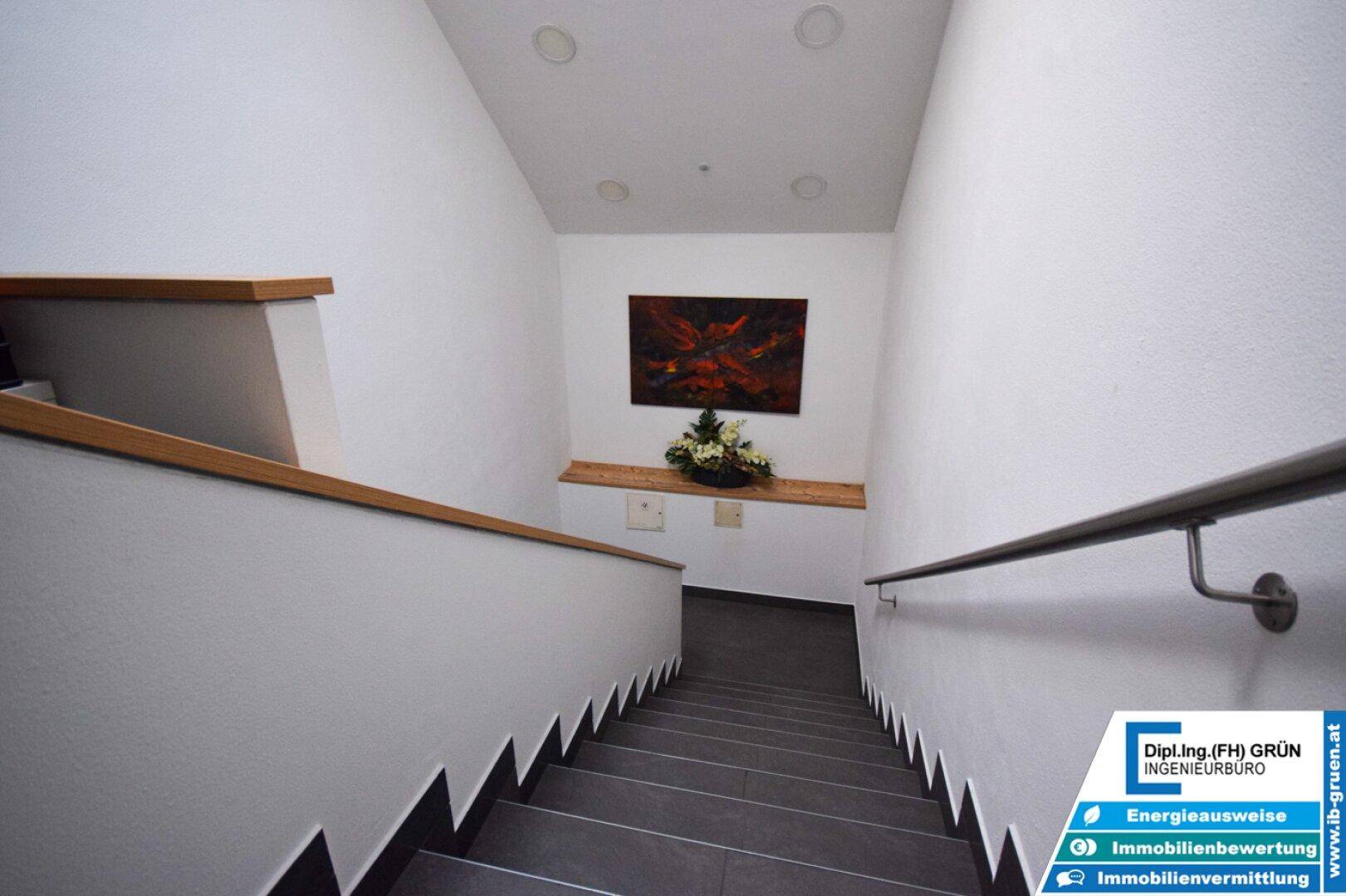 Treppenhaus mit Fliesenstufen, Holzhandlauf und moderner Wanddekoration.