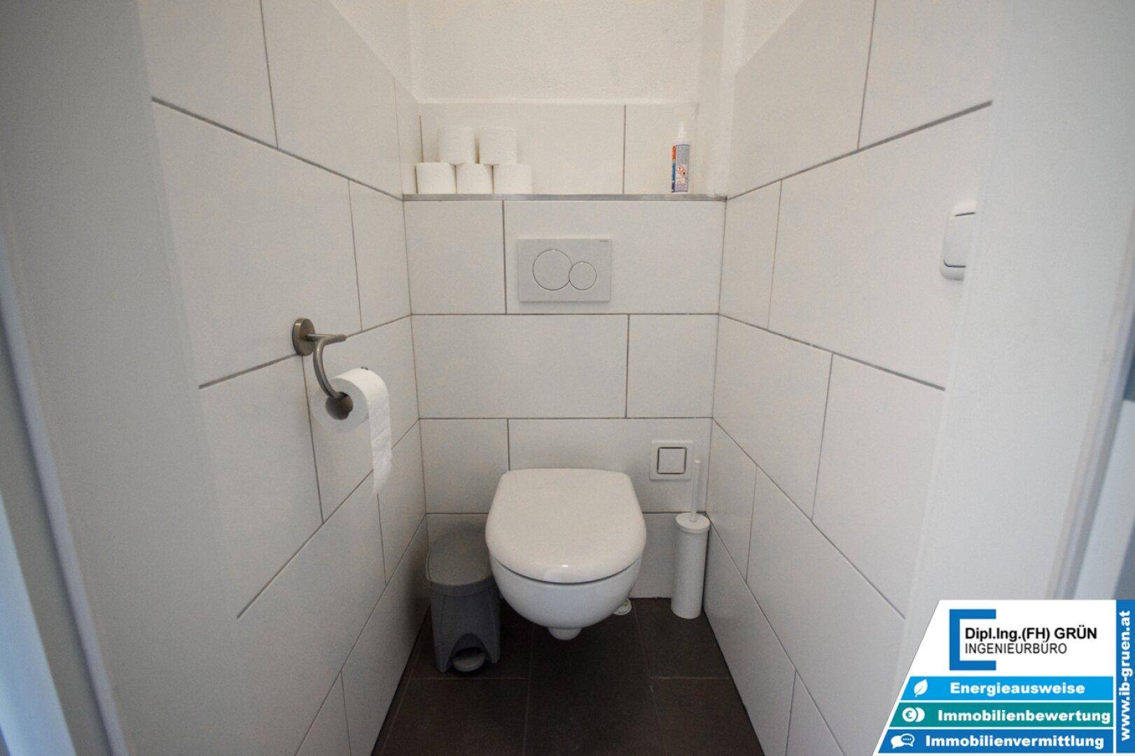 Saubere und moderne Toilette mit weißen Fliesen, Wand-WC und kleinem Mülleimer.