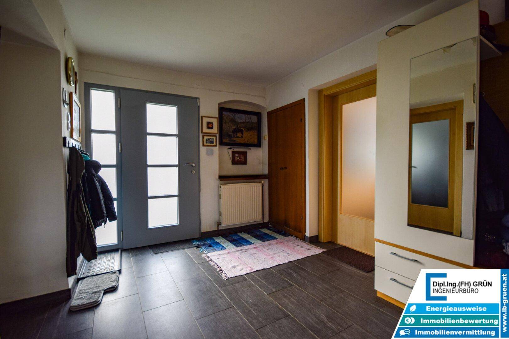 Heller Eingangsbereich mit dunklen Fliesen, Garderobe und Zugang zu weiteren Räumen.