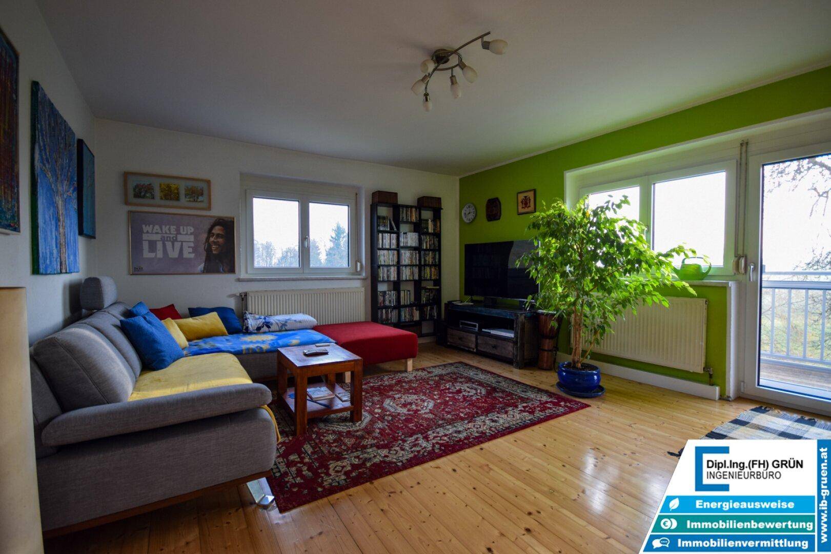 Helles Wohnzimmer mit Holzboden, grüner Akzentwand und Zugang zu einem Balkon.
