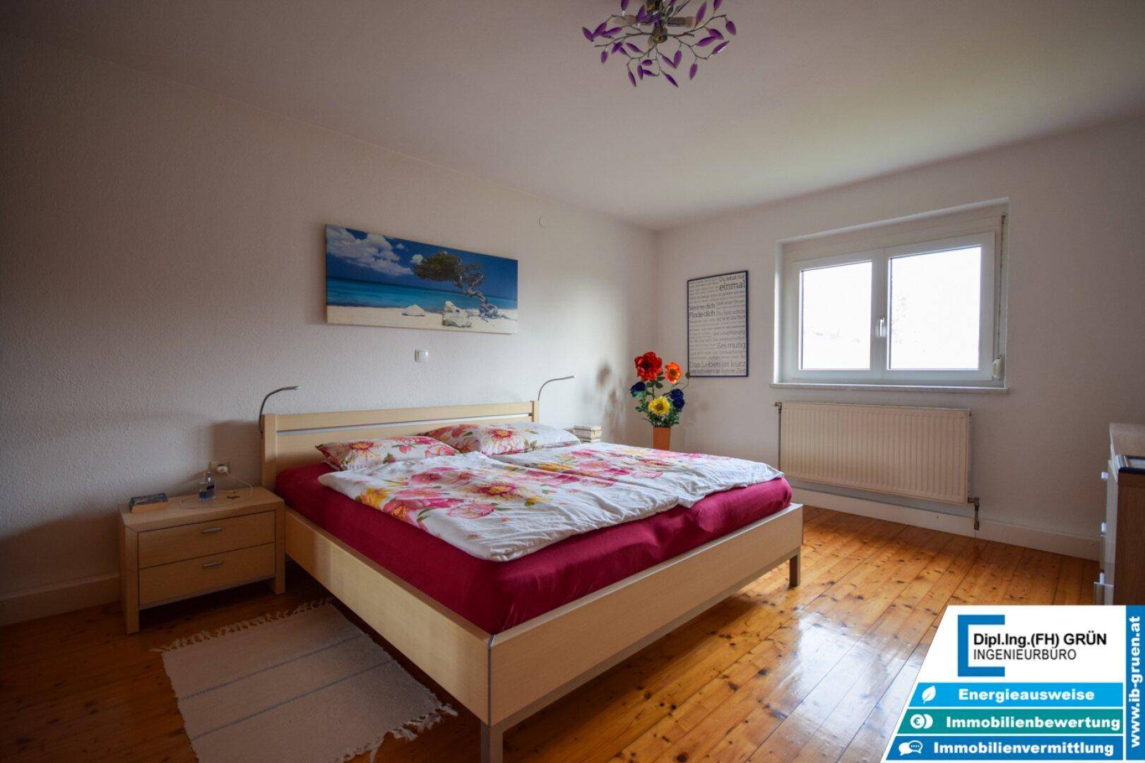 Helles Schlafzimmer mit Doppelbett, Holzboden und einem Fenster mit Blick ins Grüne.