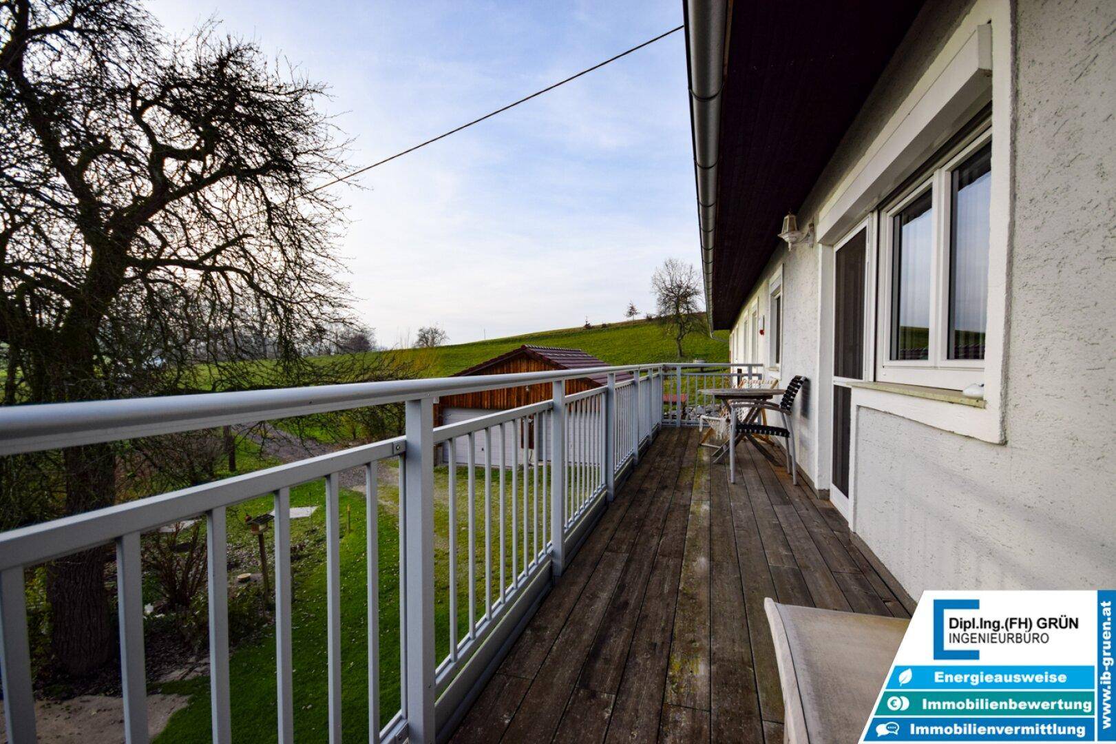 Langer Holzbalkon mit Metallgeländer und Blick auf die ländliche Umgebung.