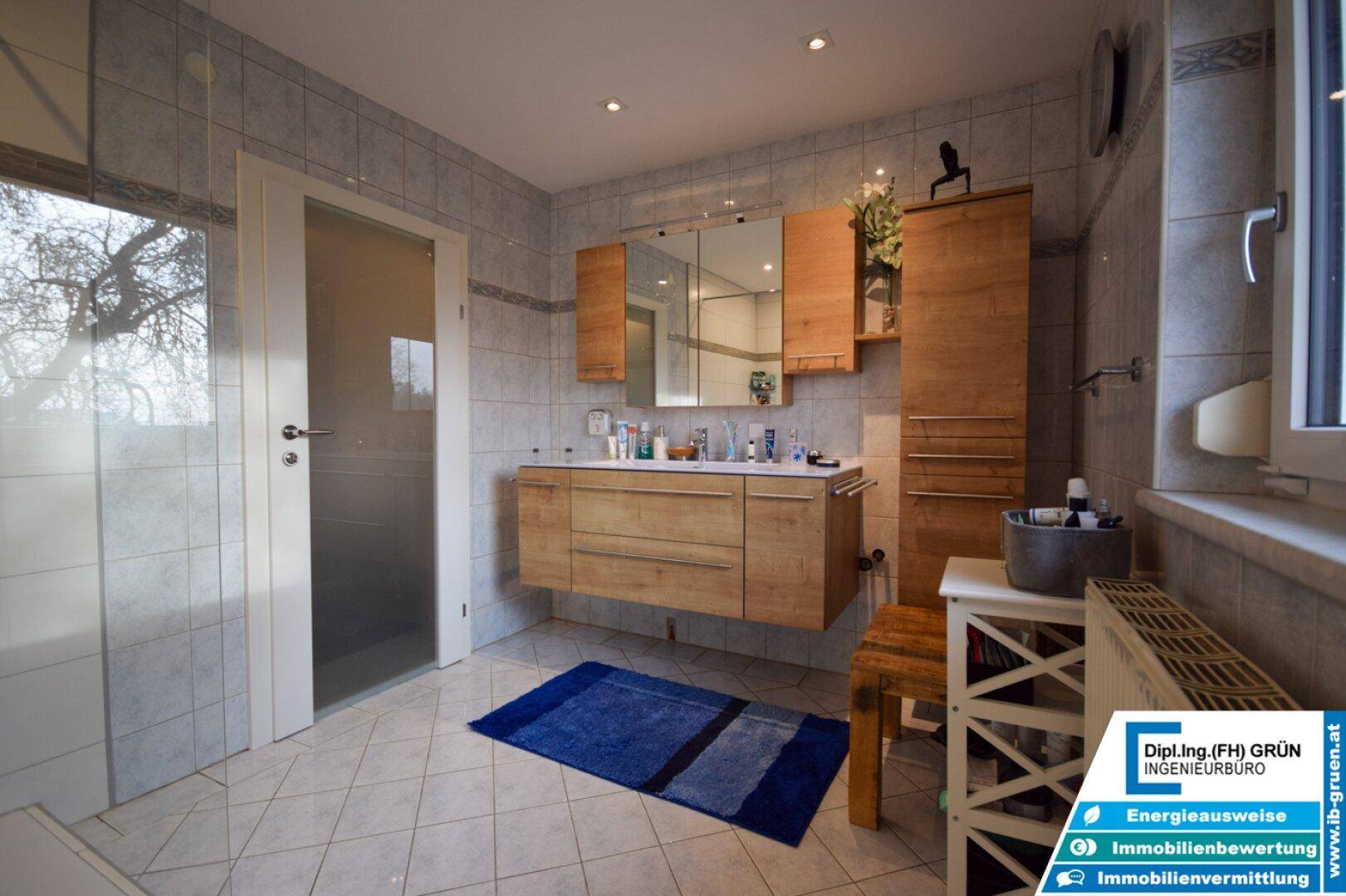 Geräumiges Badezimmer mit Holzmöbeln, Doppelwaschbecken und hellen Fliesen.