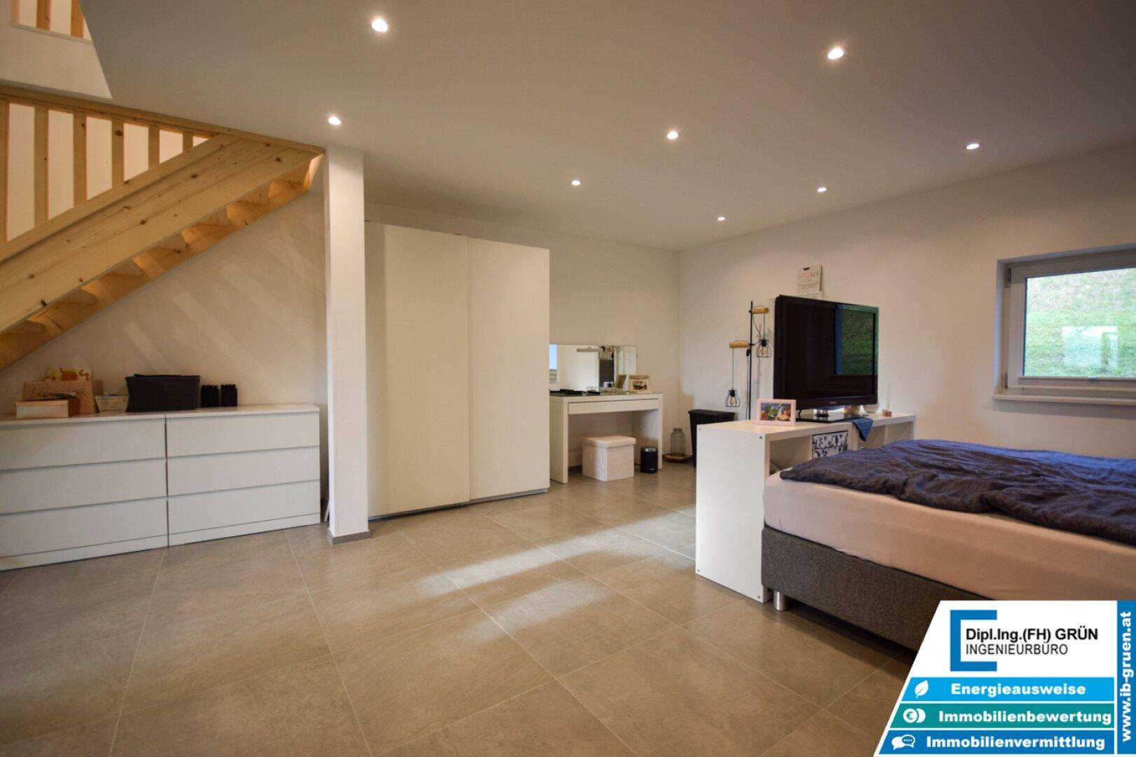 Geräumiges Schlafzimmer mit hellem Fliesenboden, Einbauschränken und Zugang zu einer Holztreppe.
