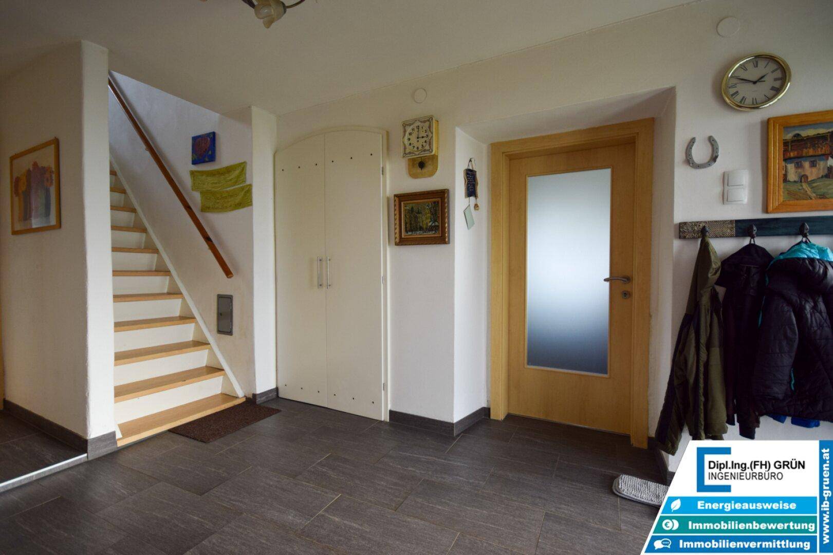 Heller Eingangsbereich mit dunklem Fliesenboden, Holztreppe und Garderobe.