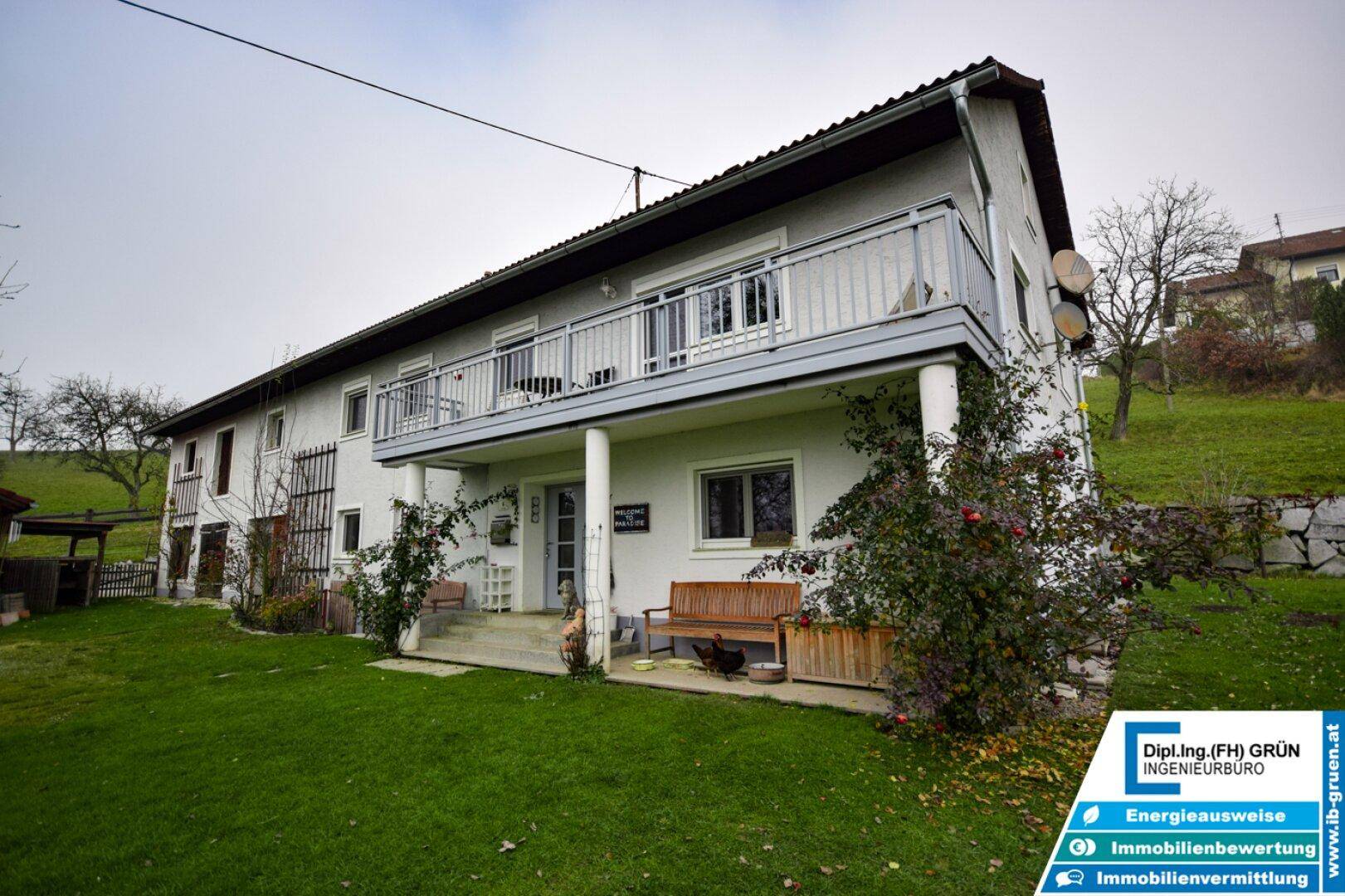 Charmantes Landhaus mit großem Balkon und überdachtem Eingangsbereich, umgeben von einem grünen Garten.