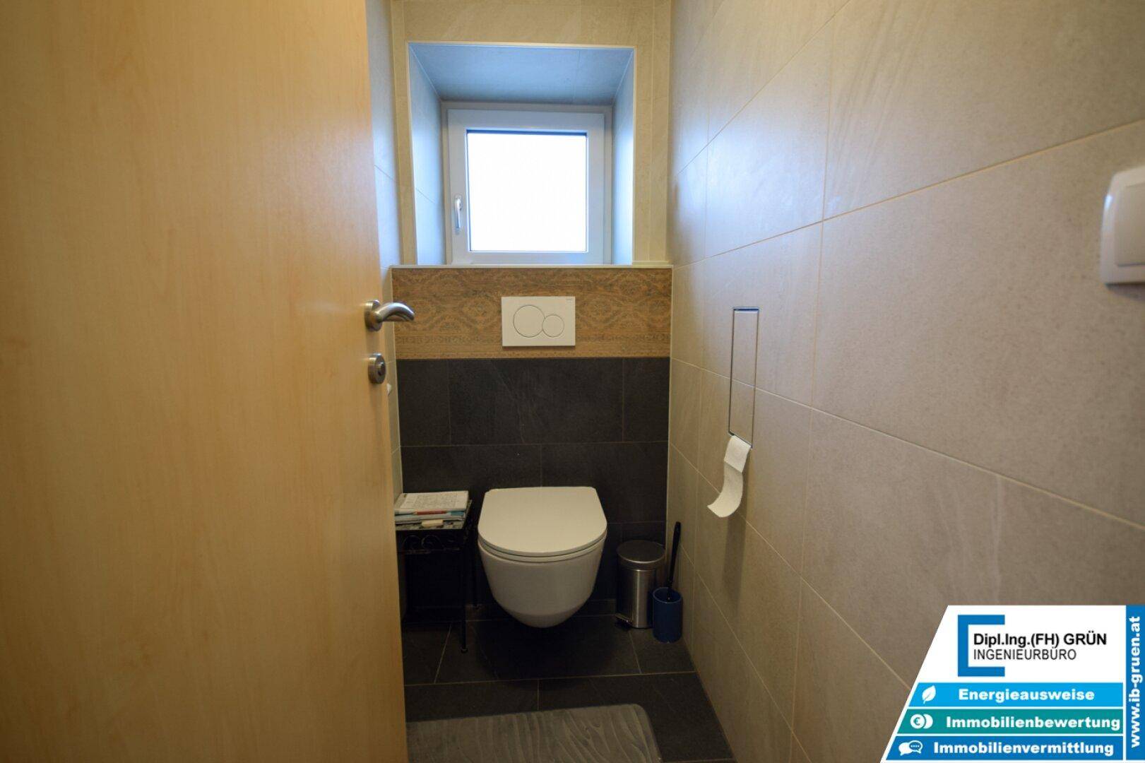 Modernes Gäste-WC mit Wand-WC, dunklen und hellen Fliesen sowie einem kleinen Fenster.