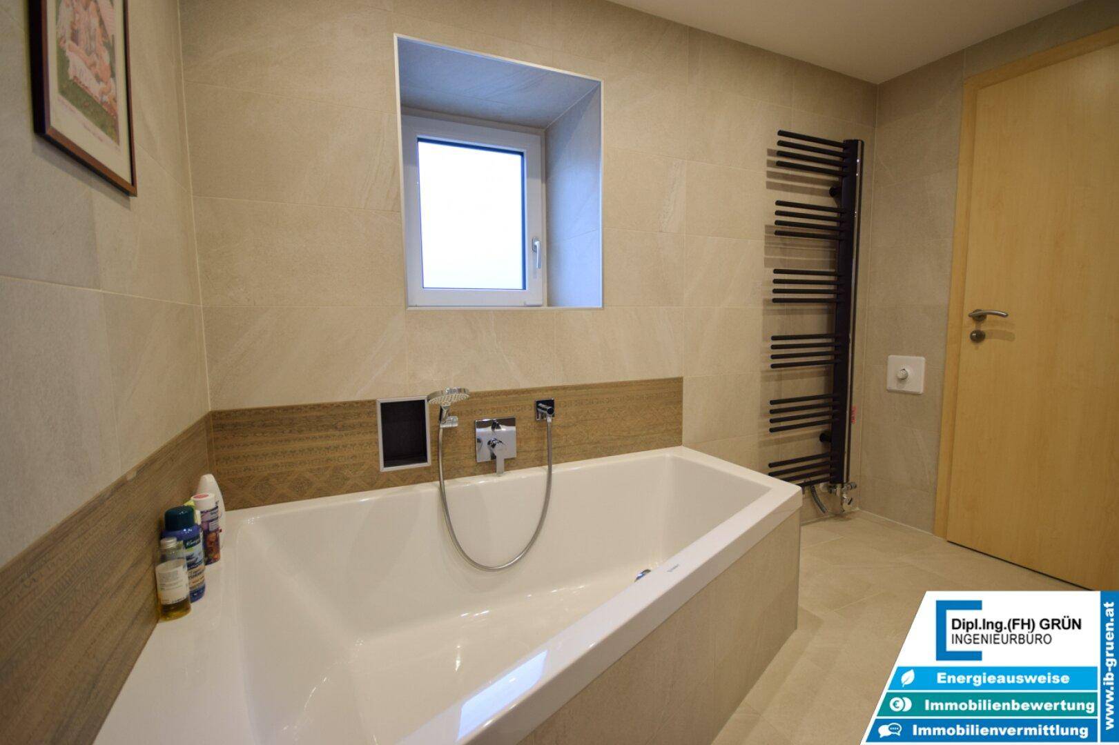 Helles Badezimmer mit Badewanne, Fenster und beheiztem Handtuchhalter.