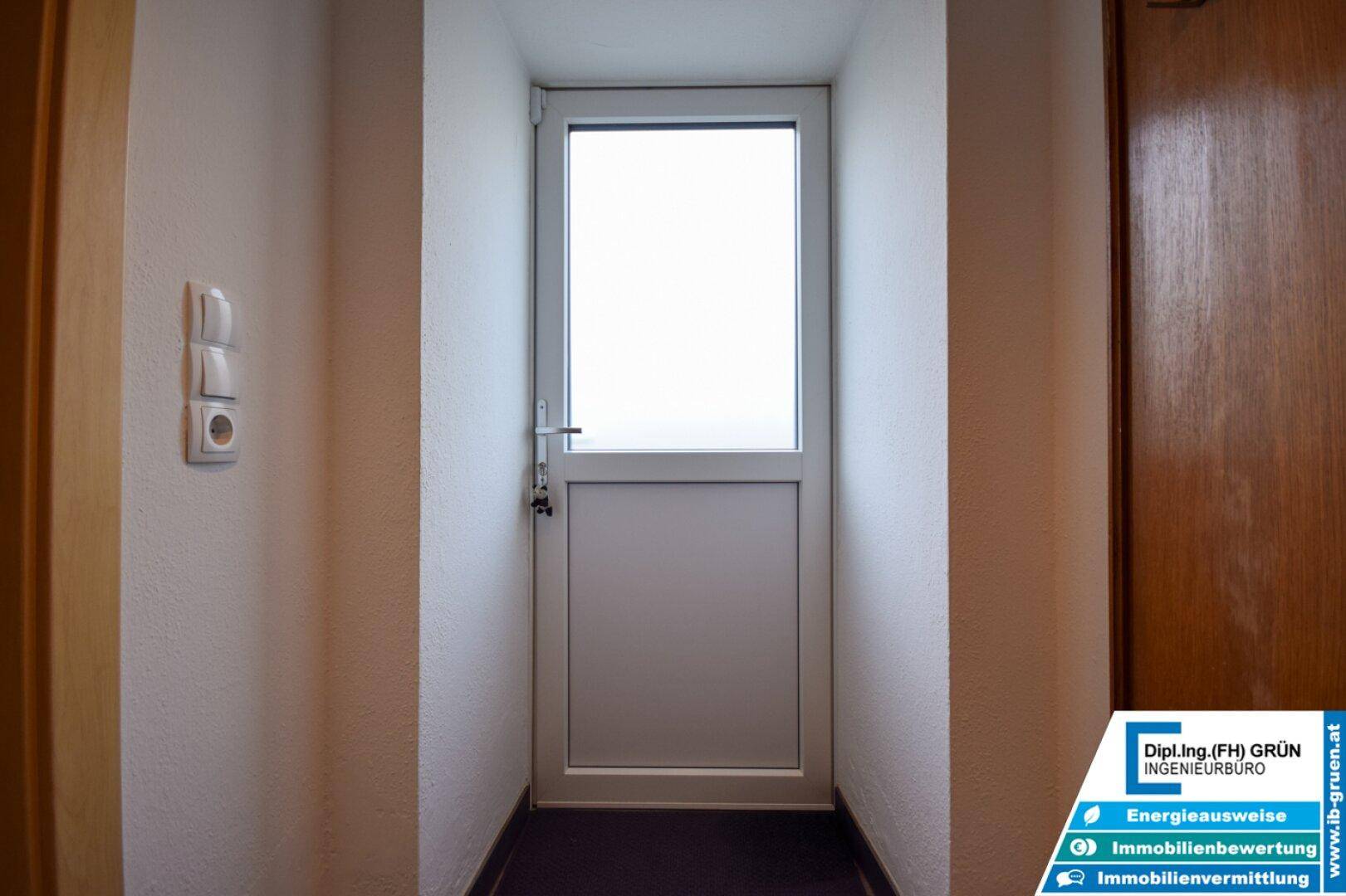 Heller Flur mit weißer Tür und Fenster, der zu weiteren Räumen führt.