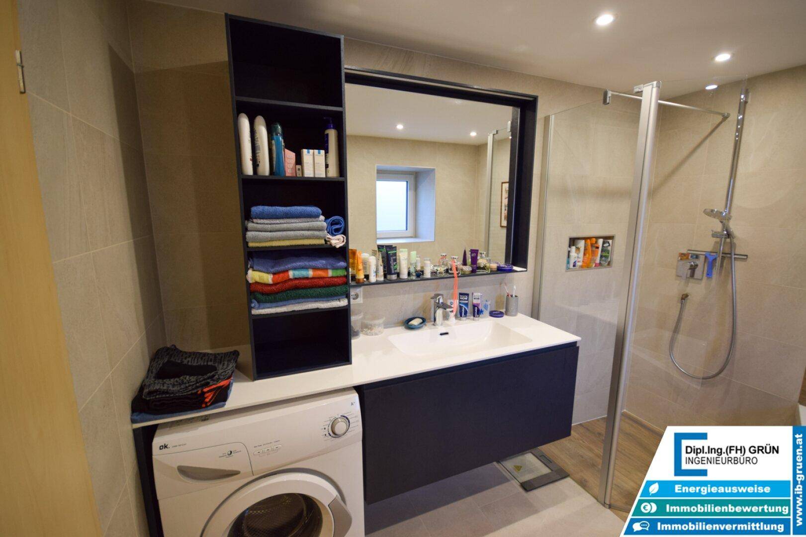 Modernes Badezimmer mit Waschbecken, Spiegel, Duschkabine und Waschmaschine.