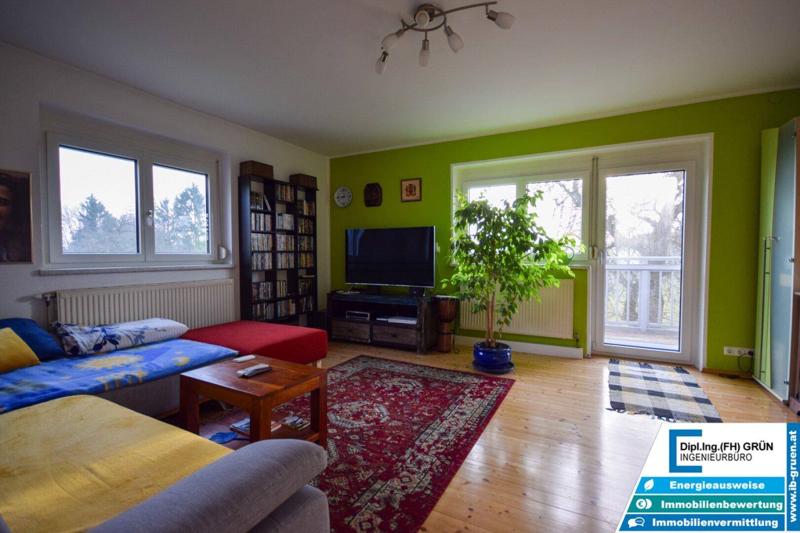 Gemütliches Wohnzimmer mit grün gestrichenen Wänden, Holzboden und Zugang zum Balkon.