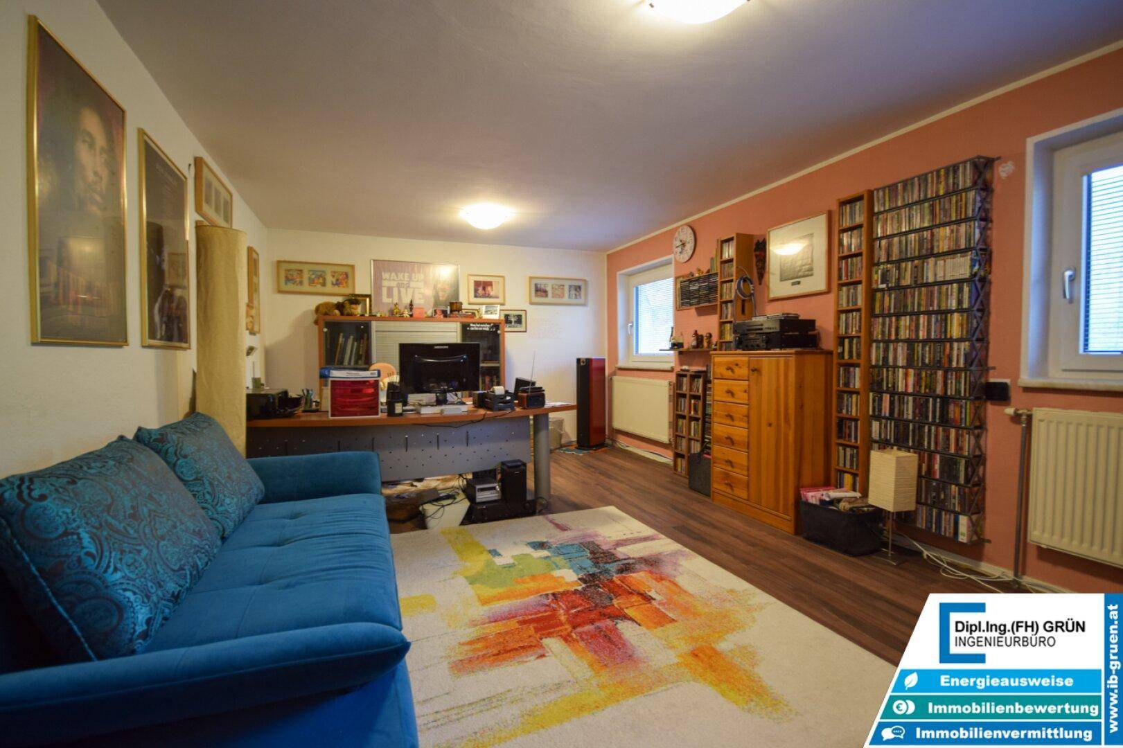 Arbeitszimmer mit blauem Sofa, Schreibtisch und Regalen voller Medien, ideal für Home-Office oder Hobby.