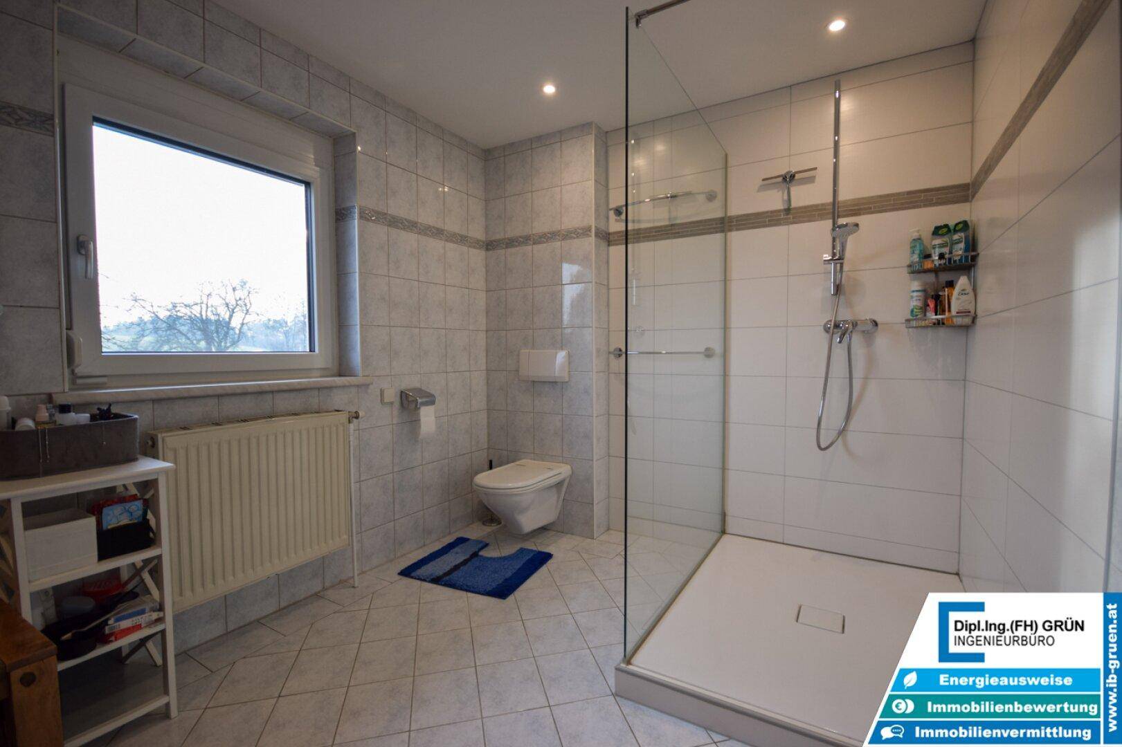 Modernes Badezimmer mit hellen Fliesen, großer begehbarer Dusche und Fenster für Tageslicht.