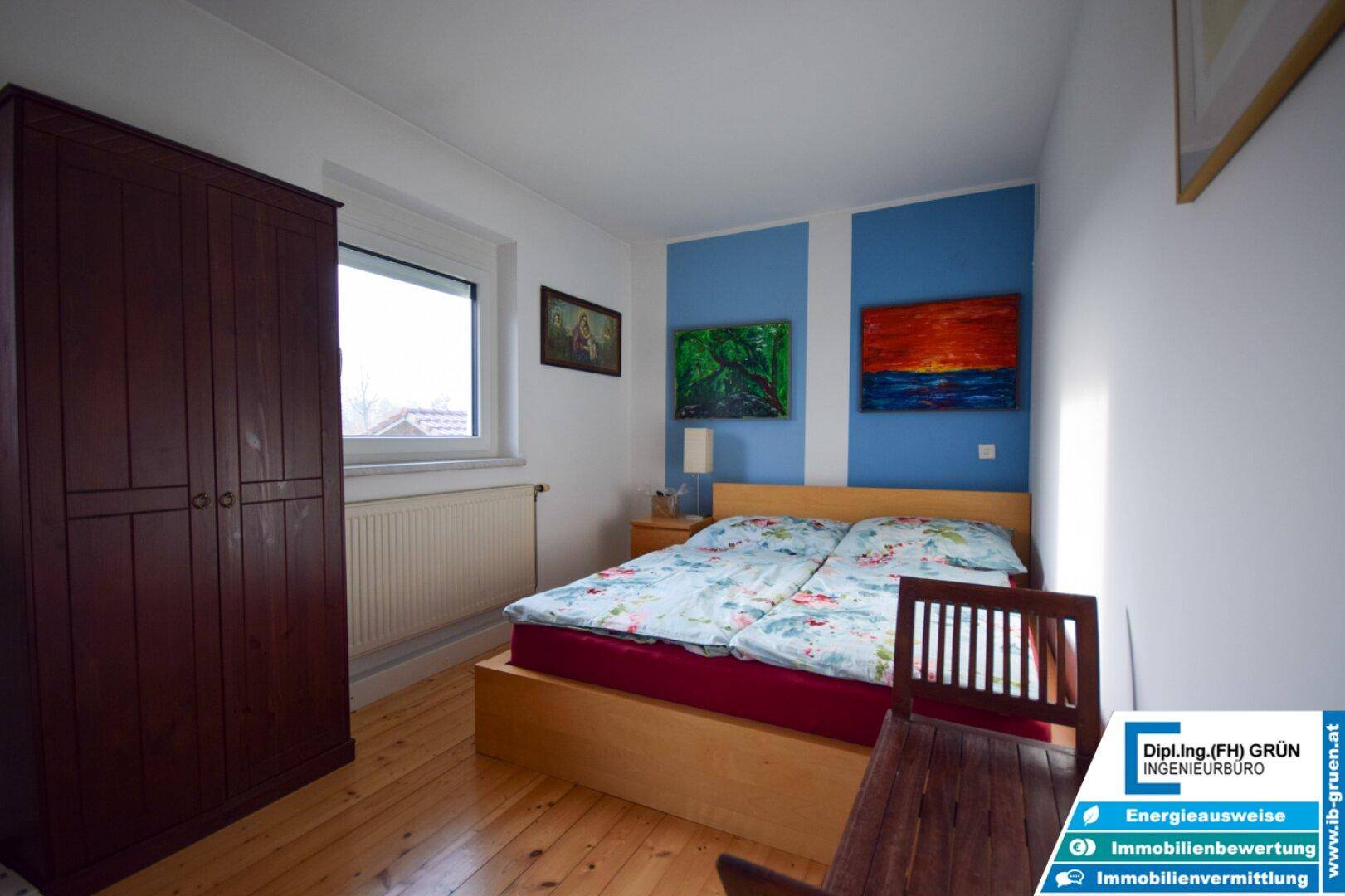 Schlafzimmer mit Holzboden, Doppelbett und farblich abgesetzten blauen Wänden, bietet eine gemütliche Atmosphäre.